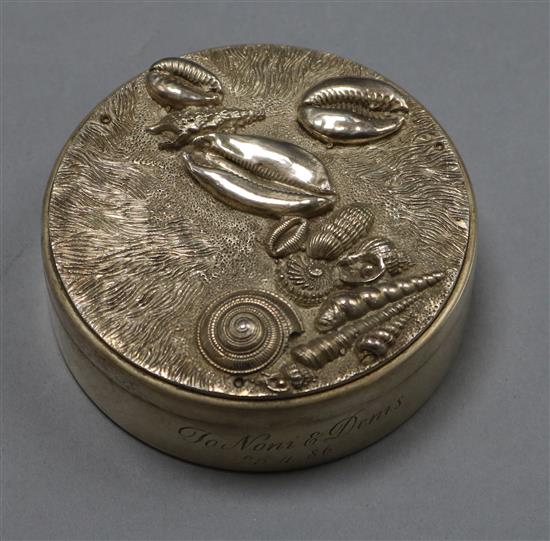 A circular silver box and cover, the latter with sea shells on a stippled and dragged ground.